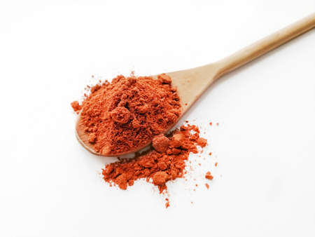 Red pepper powder in a wooden spoon on a white background. Next to the spoon crumbled pepper.の写真素材