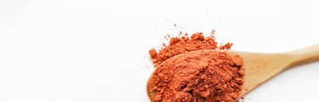 On a white background, red hot pepper in a wooden spoon. Red pepper, paprika spills out of a wooden...