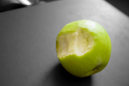 Bright apple and gray background. Black and white background and a green, bitten apple. A bitten...