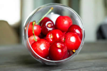 Berries of cherries in a crystal glass are on the table. On the table is an inverted glass of...