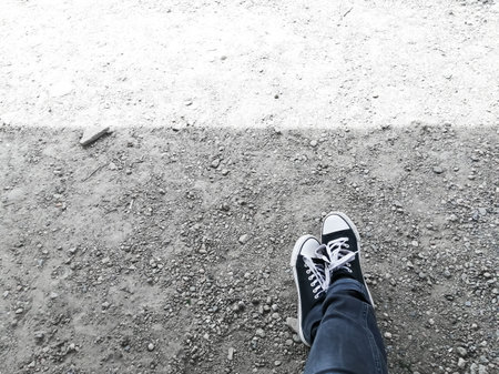 Crossed legs in sneakers on the ground. The sun illuminates the earth making a flat stripe, and on the side crossed legs. Legs in jeans. Sneakers, foot to foot.の写真素材