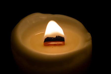 A close-up of a burning candle. the candle burns in a dark room. black background. Candle with wooden fetil. wooden board in a candle. a big fire in the night.の写真素材