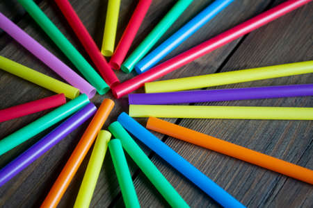 Many colorful straws for drinks lie on a wooden table. A circle of tubes. Plastic straws in the form...