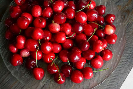 Lots of red cherries on a glass plate. Wooden table and glass plate with cherry. Cherry season -...