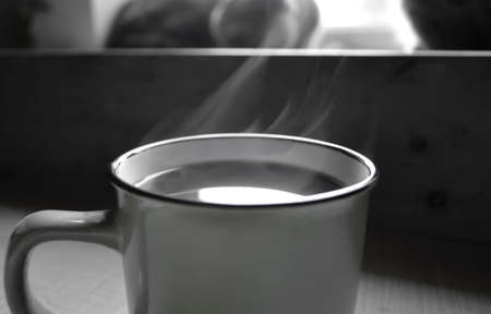 A hot drink cup in gray tones. Steam comes from the cup. There is soft smoke coming from a cup of coffee. Gentle smoke - black and white photo.の写真素材