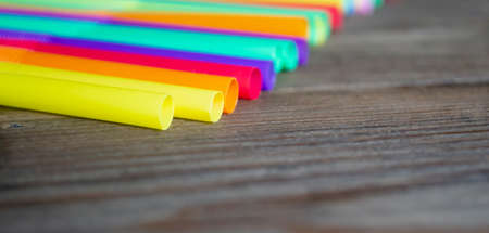 Colored plastic straws lie on a wooden table in a row. A row of colored cocktail straws. wooden background and plastic straws for drinks. Cocktail straws.の写真素材