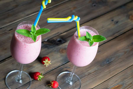 Strawberry cocktails with sprigs of mint. The glasses have two woven straws. yellow-blue tubes are a symbol of Ukraine. Strawberries on the table, next to the bcals. Summer cocktails with straws.の写真素材