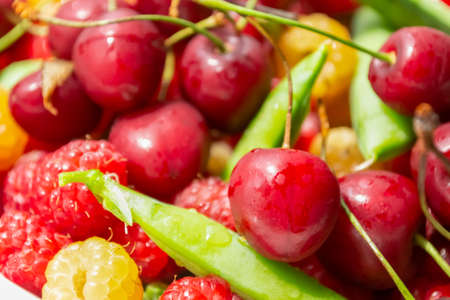 Cherries, raspberries and green peas in pods. Summer berries in a heap. Lots of summer berries. Fresh berries - cherries and raspberries, green peas.の写真素材