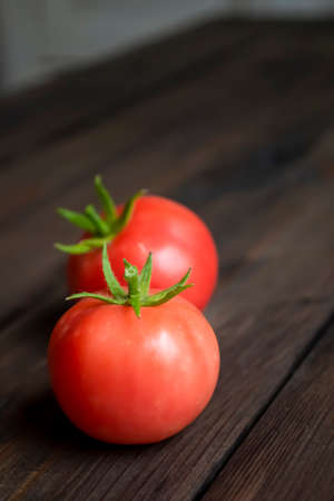 Two tomatoes on a wooden table. On the table are two red tomatoes with tails. green crappie on red tomatoes. The first harvest of tomatoes.の写真素材