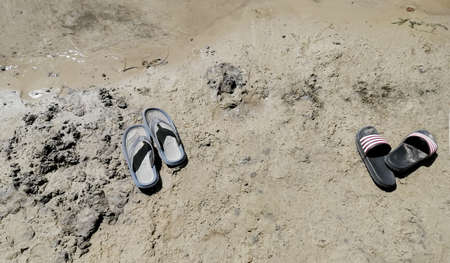 ON wet sand rubber slippers. spanking in the sand. spanking on the beach. Beach shoes on the sand. Two pairs of shoes on the sand.の写真素材