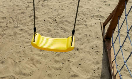 Yellow swing seat. children's swing with yellow seat. Children's playground on the sand. There is yellow sand under the children's couch.の写真素材