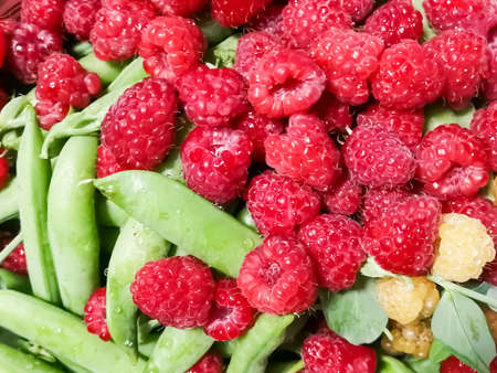 Lots of bright berries and green peas. Summer berries together. Raspberries, green peas in pods.の写真素材