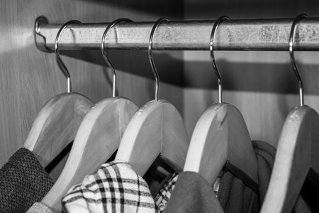 Hangers with clothes hang in the closet. Black and white photo of a hanger in a closet with clothes. Things hang on wooden hangers.の写真素材