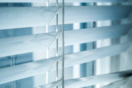 The window is visible through the open blinds. white blinds. Photos of blinds with a blue tint.の写真素材