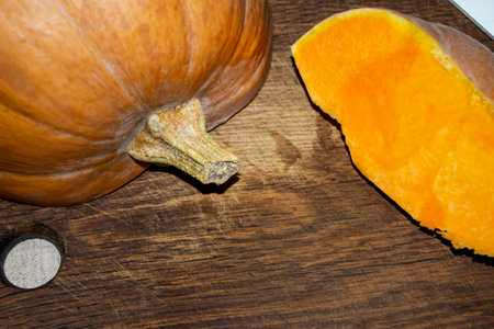 Cutting a pumpkin on a wooden board. A pumpkin with a tail lies on the board. Orange pumpkin nearby.の写真素材