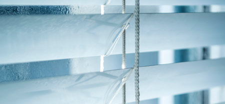 The window is visible through the open blinds. Photos of blinds with a blue tint. white blinds.の写真素材