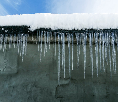 Large icicles hang from the roof of the house. Dangerous icicles in winter on the house. Long frost icicles in winter.の写真素材
