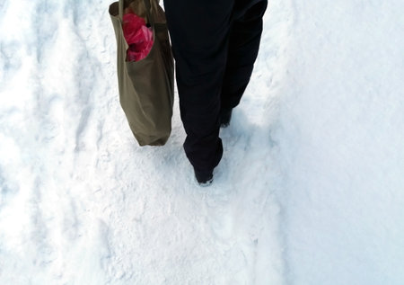 human legs and shopping bag. a man walks through the snow with a full bag. Bag of groceries - the feet of a man in black pants walk through the snow.の写真素材