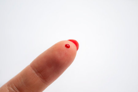 A drop of blood on the index finger. white background - a drop of blood on the finger. A red drop of...
