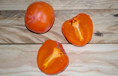 On the wooden table is a persimmon. A cut persimmon and a whole one lie on the table. Winter fruit - persimmon. halves of persimmons, view from above.の写真素材