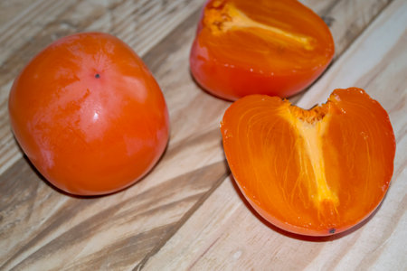 On the wooden table is a persimmon. A cut persimmon and a whole one lie on the table. Winter fruit - persimmon. halves of persimmons, view from above.の写真素材