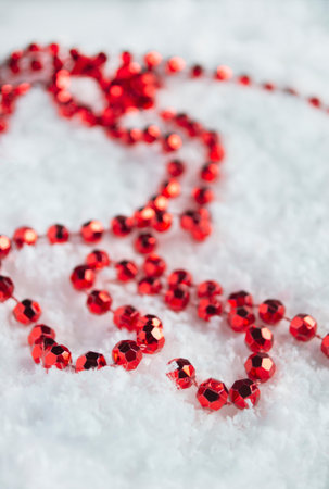 Festive beads in the snow. Decorations for Christmas and New Year are red beads. Christmas beads on the tree lie on the white snow. vertical photoの写真素材