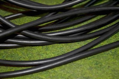 Black wire on the green carpet. A thick wire of black color in a winding on a green carpet. There is a reeled black cable on the floor.の写真素材