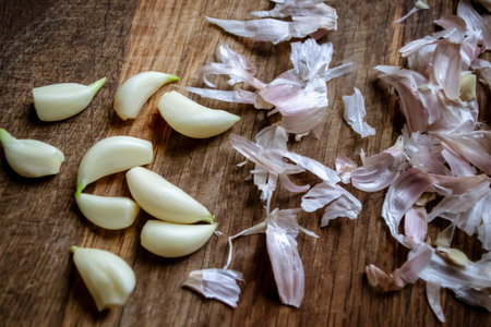 Peeled garlic lies next to the husks on the table. On a wooden table is garlic and husks. Peeling cloves of garlic. Peeled garlic on the table.の写真素材