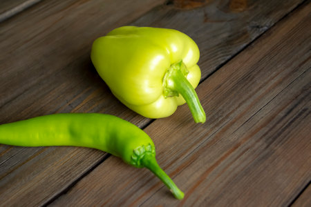 Sweet and hot peppers on a wooden table. On the table are two types of pepper - green chili and green bell.の写真素材
