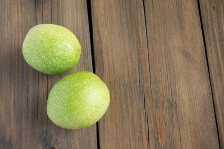 A young walnut in a green skin. Two walnuts in a green skin on a wooden table. two walnuts.の写真素材