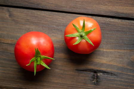 Two red tomatoes with green tails on a wooden table. On a wooden background lies two ripe tomatoes. Red tomatoes are a healthy food with bright-zedun peduncles.の写真素材