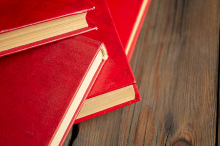 Books with a red cover lie a together. Piled up books on the learning table. On the wooden table are many books with a red cover.の写真素材