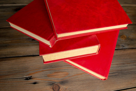 A lot of books with a red cover. Red books on the table. Books are piled up on a wooden table.の写真素材