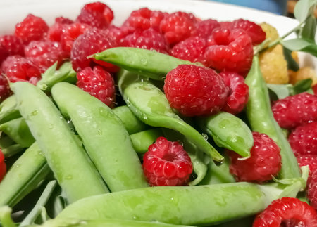 Fresh, summer berries - green peas in pods and red raspberries. Green peas are in the same bowl with red raspberries. Healthy legumes are in the summer.の写真素材