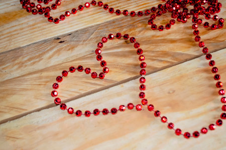The heart is lined with red beads on a wooden table. A heart is lined with beads on the table. Valentine's Day - valentine on the table with your own hands.の写真素材