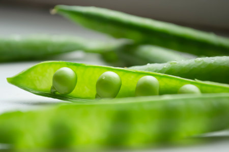 Green peas on the table. On a white background is an open pod of green peas. Green pea pods with young beans.の写真素材