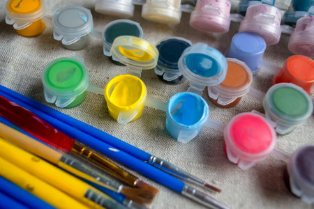 Paints on the table next to the brushes. Yellow and blue paints on the table in jars. Watercolor paints for drawing and brushes.の写真素材