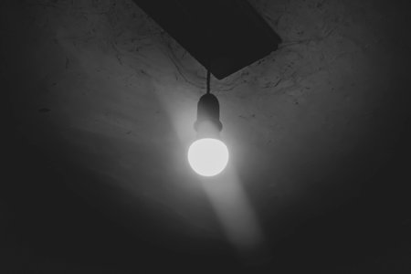 A light bulb is on in a dark basement. One light bulb on the ceiling. The ominous atmosphere is a light bulb in a dark room.の写真素材
