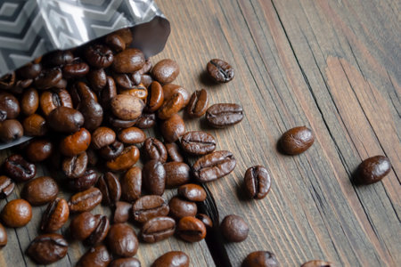 Beans poured out of the coffee bag. Coffee beans on the table next to the package. fresh coffee. New packaging of coffee beans.の写真素材