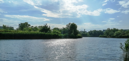 There is a cloudy sky over the river. Along the river grows reeds and trees. Beautiful sky over the river.の写真素材