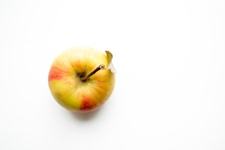 One apple on a white background. An apple with a ponytail on the table. Yellow apple with red spots. Apple - shooting from above.の写真素材