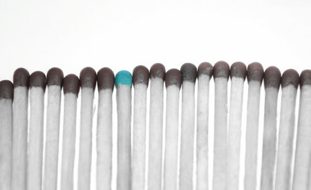 A row of dark matches and one blue. One bright match in a gray row. color selection - a horizontal photo with muted tones. The only blue match in a row of browns.の写真素材
