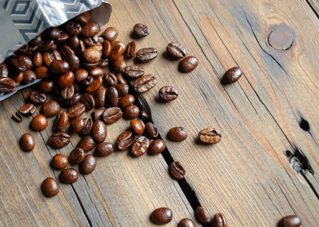 Coffee beans are scattered around the table. Arabica coffee beans poured out of the bag onto a wooden table. Fresh coffee beans from a pack.の写真素材