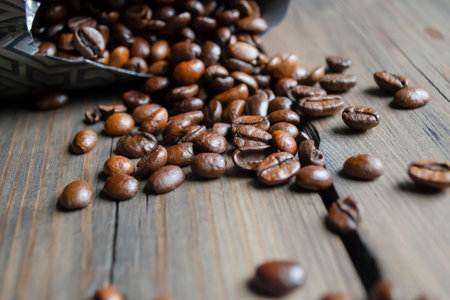 Coffee beans are scattered around the table. Fresh coffee beans from a pack. Arabica coffee beans poured out of the bag onto a wooden table.の写真素材