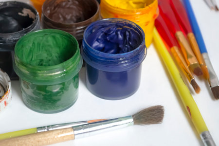 Jars of colored paint stand next to the brushes. For artists, there are a lot of paints and brushes. watercolor and oil paints on a white table.の写真素材