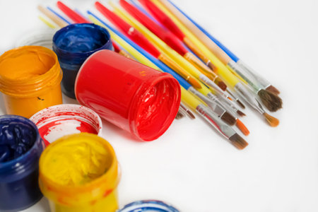 watercolor and oil paints on a white table. Jars of colored paint stand next to the brushes. For artists, there are a lot of paints and brushes.の写真素材