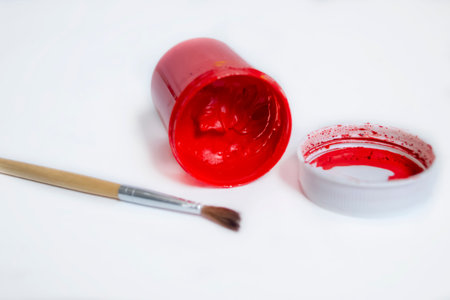 On the white table of the jar are watercolors in red. a jar of red watercolor with an open paint. An inverted can of red watercolor with a brush.の写真素材