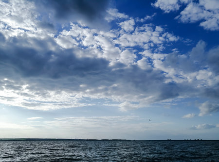 Lots of clouds in the blue sky just above the river. Beautiful sky above the water. There are curly clouds over the river.の写真素材
