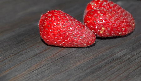 Two strawberries on a wooden table. Strawberries without tails. Dirty strawberries on a dark background.の写真素材