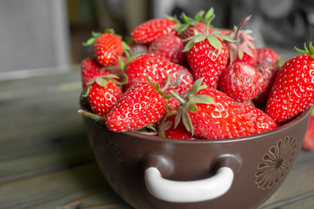 Strawberries in a bowl on a wooden table. Strawberries with green tails. The first harvest of strawberries on a plate. The first spring strawberries - useful berries from the garden.の写真素材